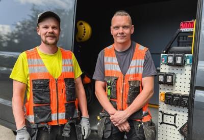 Kaksi miestä rakennnusmiehen työvaatteissa avoimen pakettiauton oven edessä.